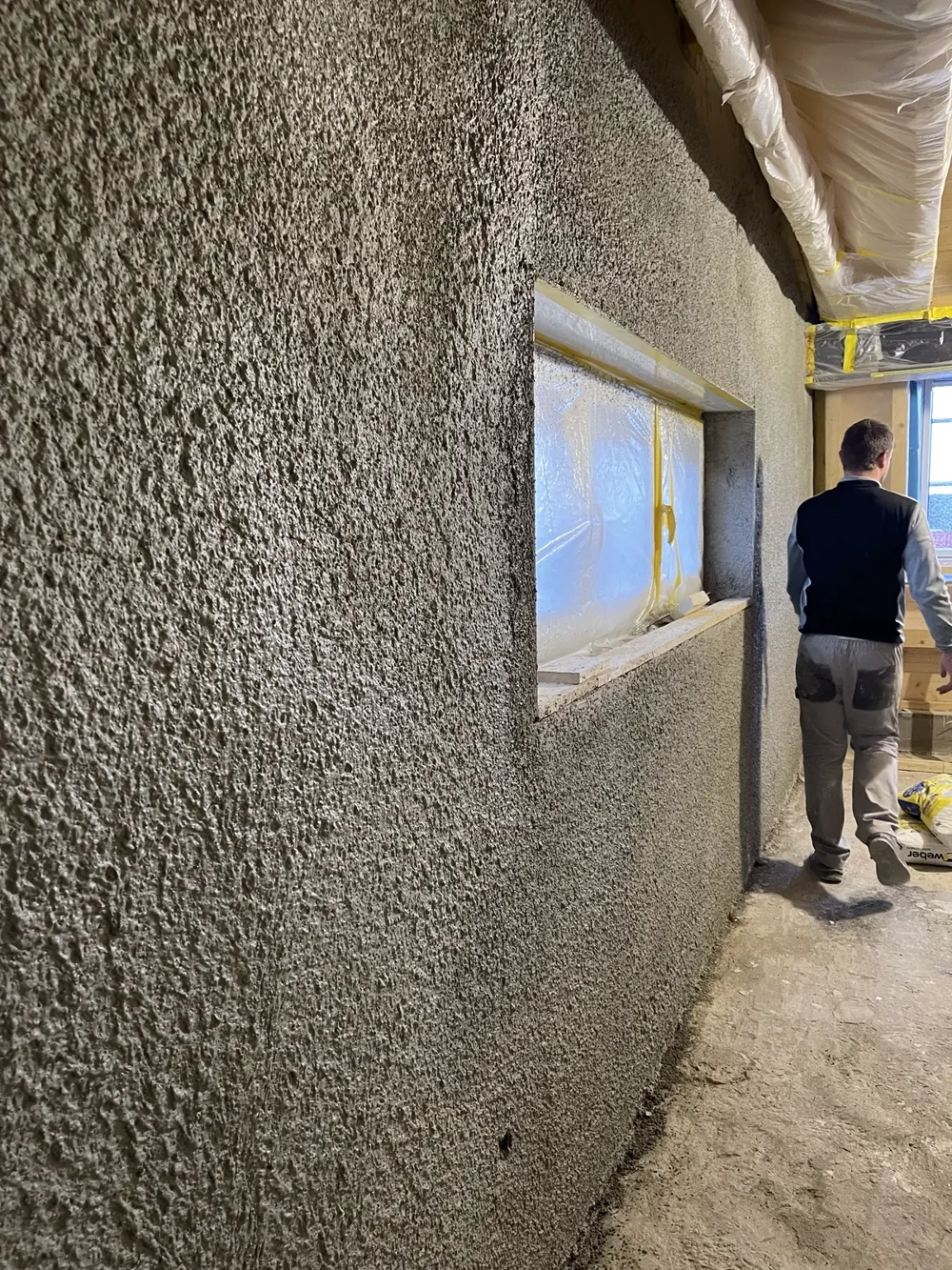 Pracownik wykonuje tynkowanie ścian wewnętrznych metodą natryskową w surowym pomieszczeniu