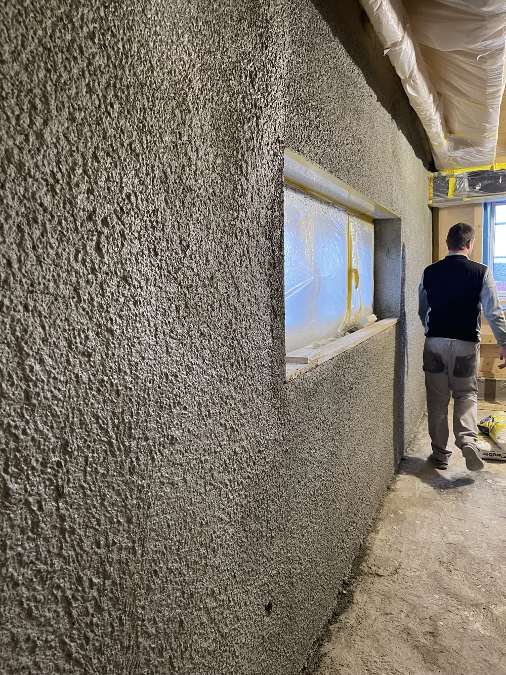Handwerker bei Putzarbeiten an verputzter Innenwand im Rohbau