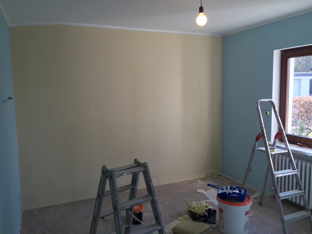 Leitern, Farbeimer und Abdeckfolie vor frisch gestrichener Wand in Beige und Blau – Malerarbeiten im Innenausbau