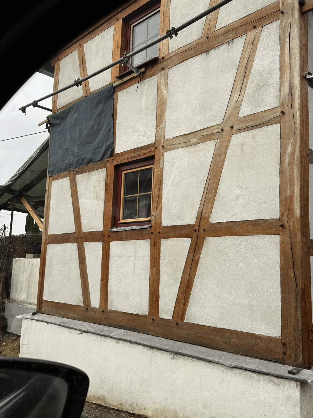 Fachwerkfassade mit frischem Außenputz zwischen Holzbalken und eingebautem Fenster, Putzarbeiten